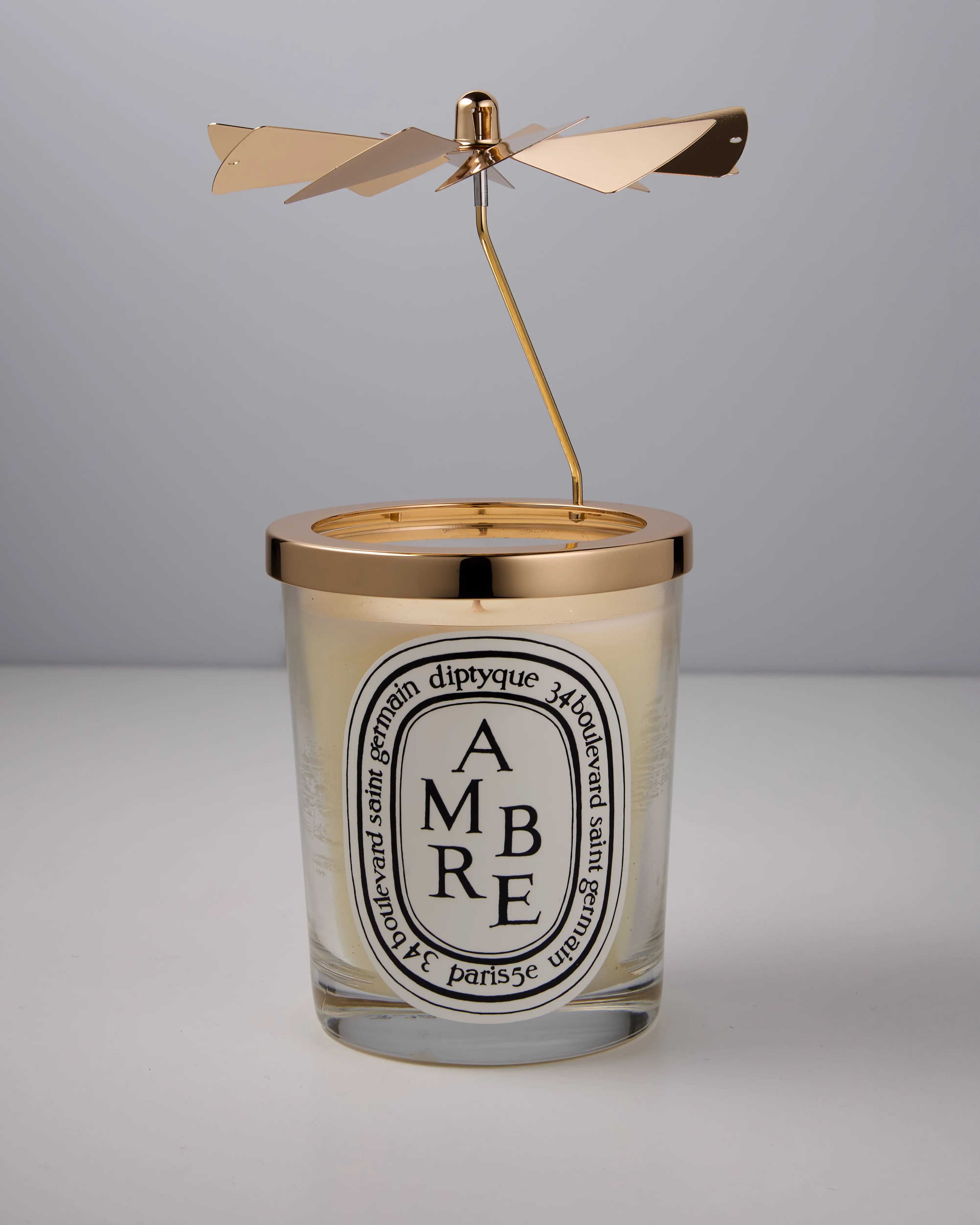 Bougie parfumée Diptyque Ambre avec un support de décoration doré tournant au-dessus.