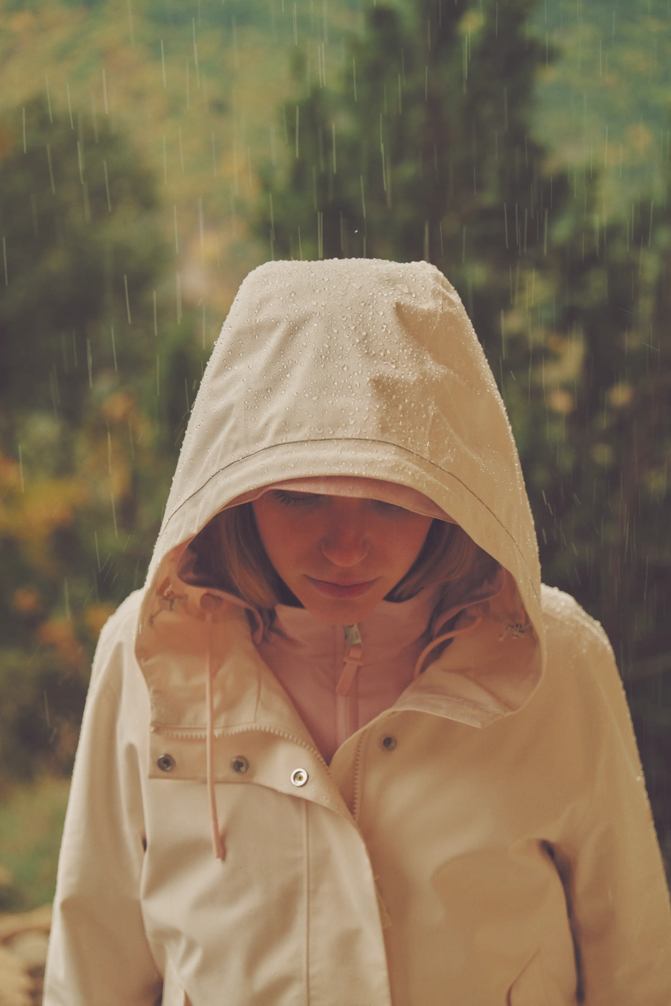 Femme avec une veste à capuche portant sous la pluie, la capuche couverte de gouttes d'eau.