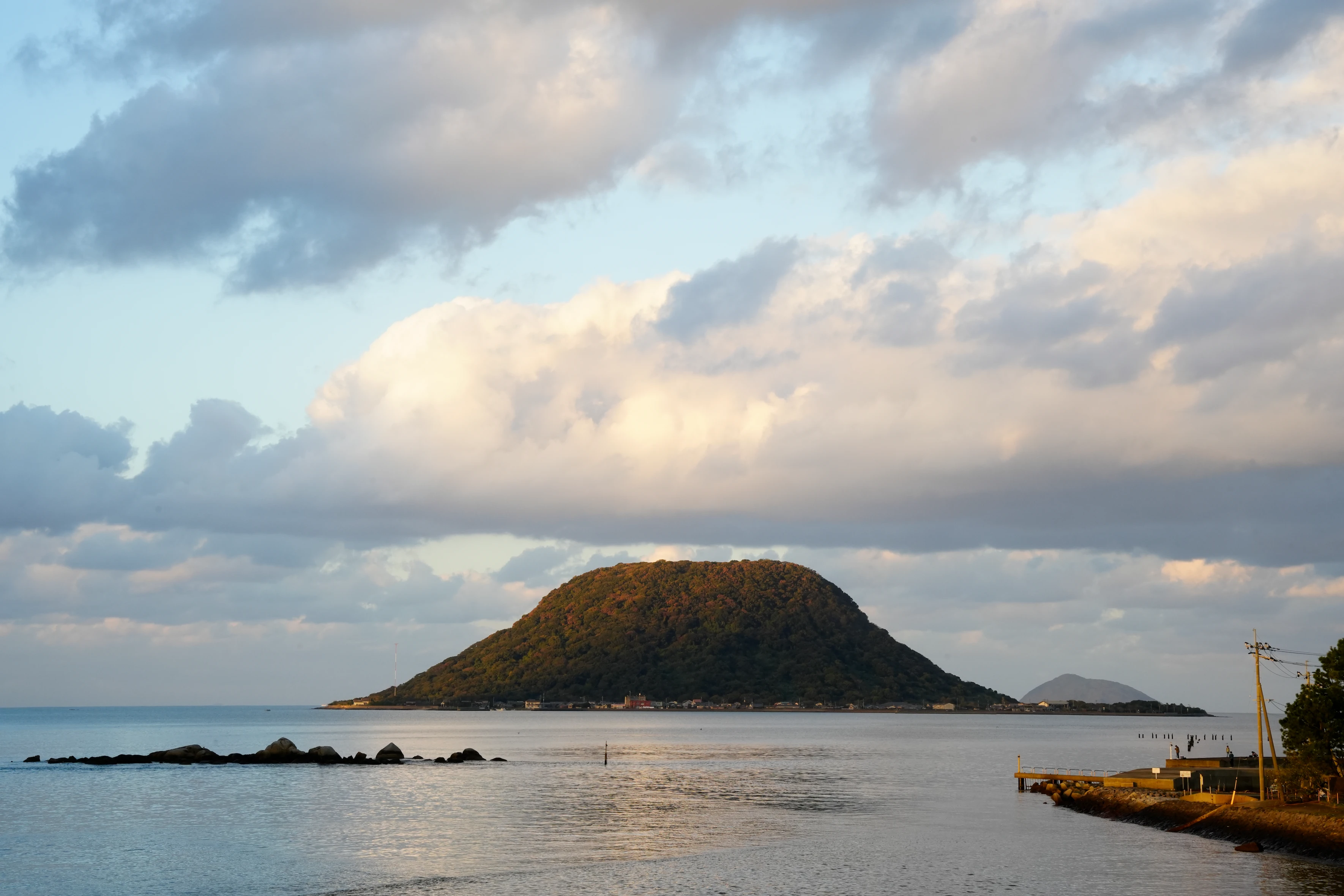 Large tree-covered island surrounded by calm water under a partly cloudy sky during sunset.