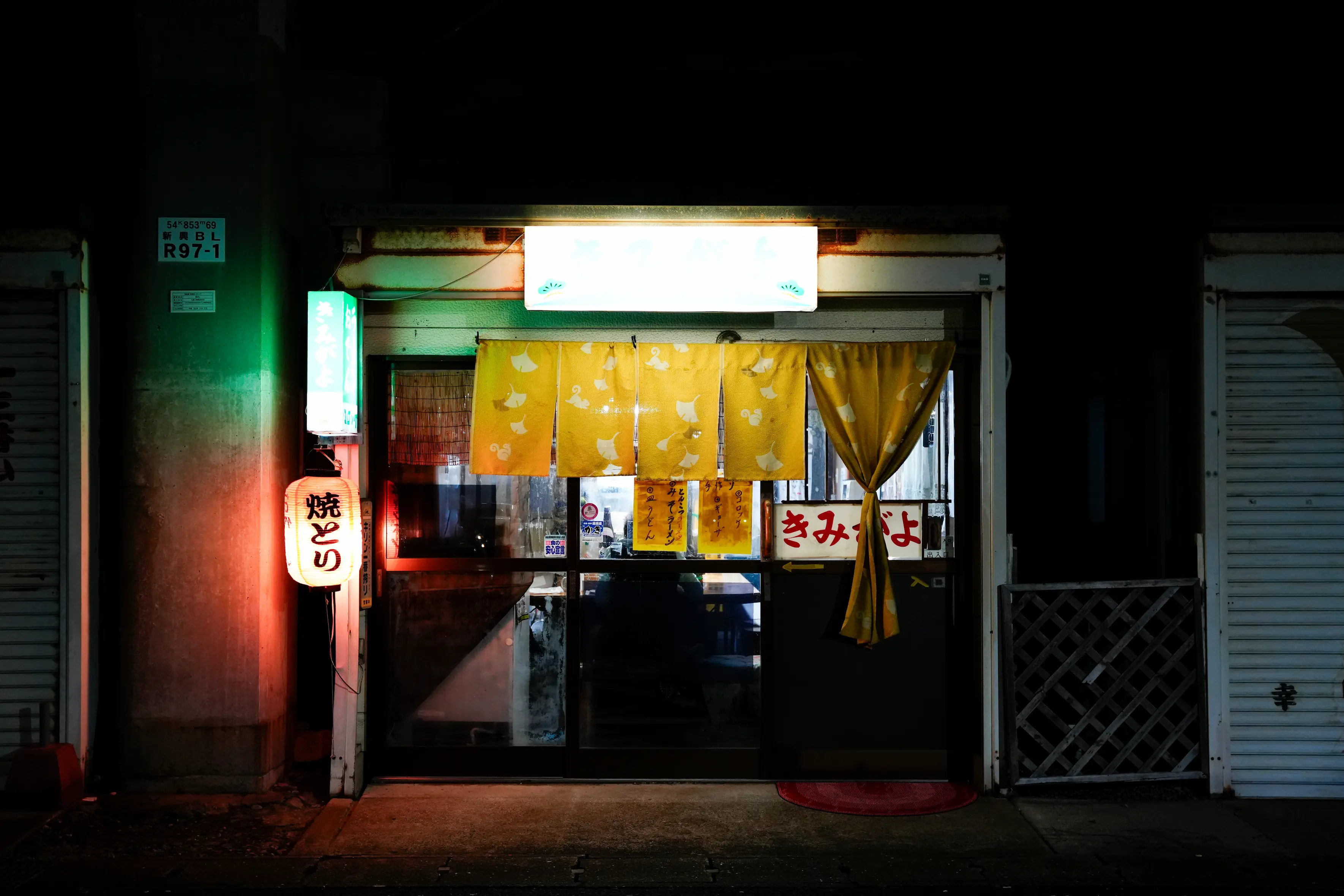 Façade d'un petit restaurant japonais éclairé la nuit avec des rideaux jaunes suspendus à l'entrée.