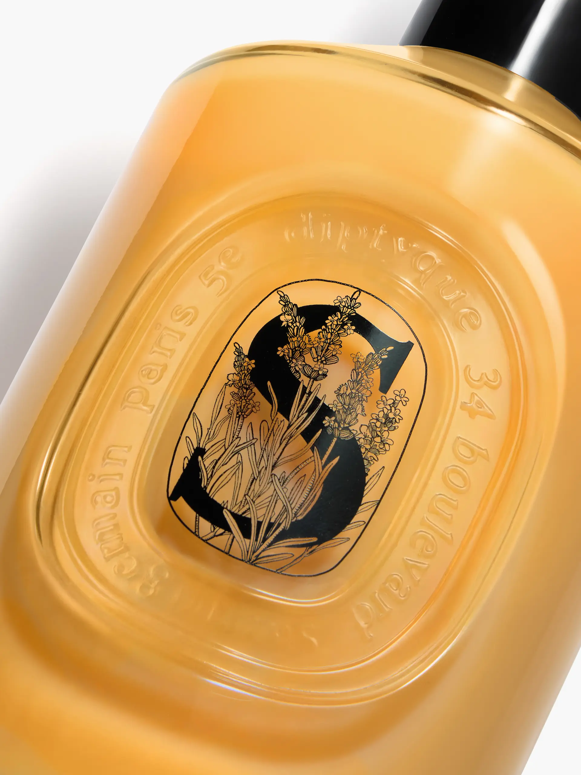 Gros plan d'un flacon de parfum jaune avec un logo noir « S » et des illustrations de fleurs.